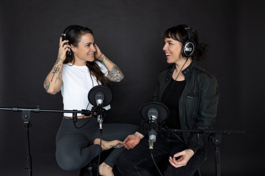 Two women wearing headphones and recording into microphones.