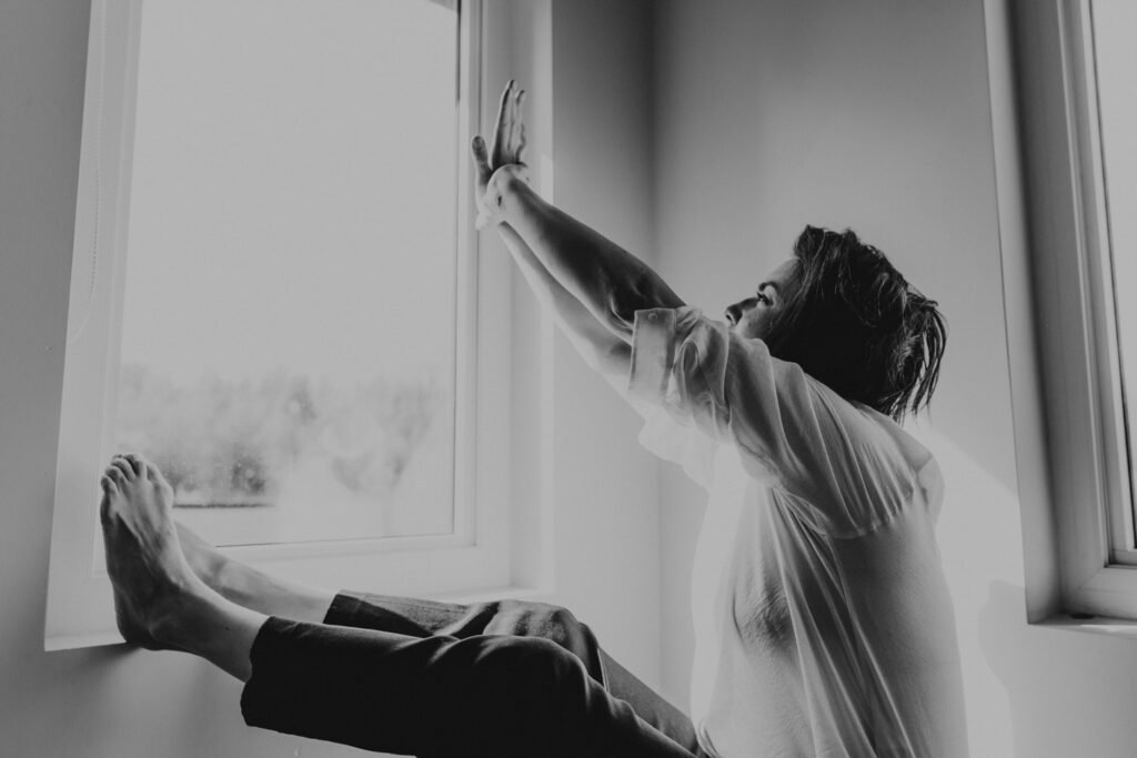Woman stretching her arms beside a bright window in black and white.