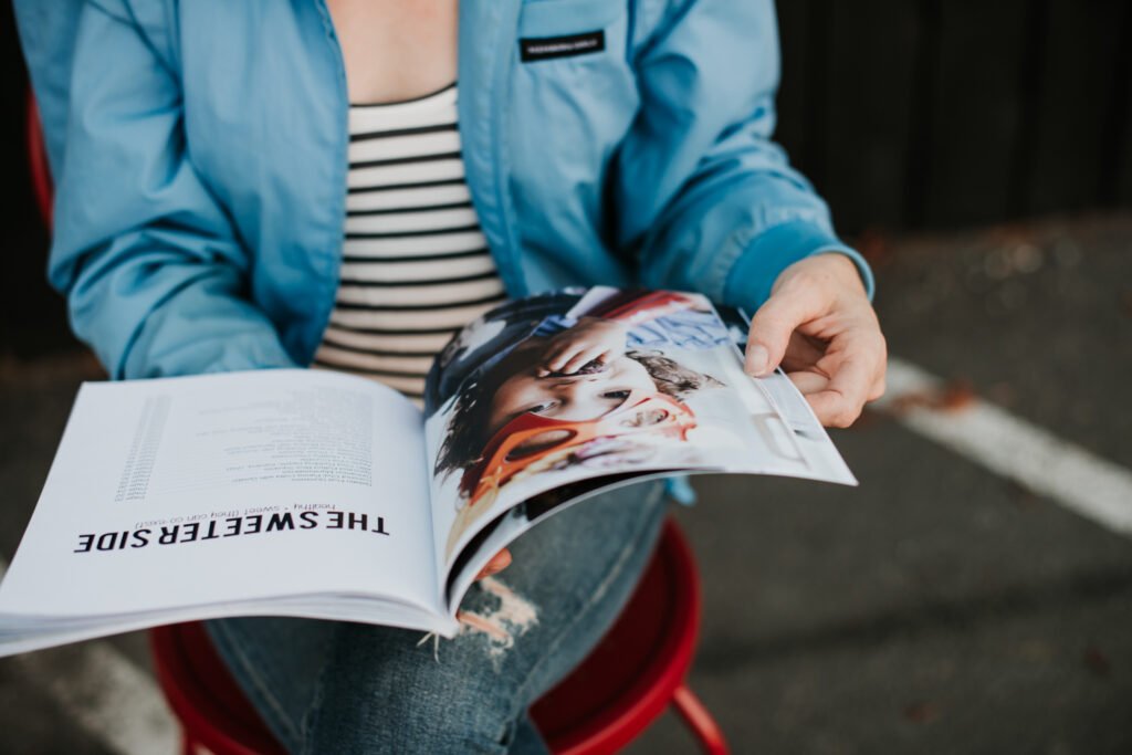 Person sitting on a red chair while reading an open magazine.