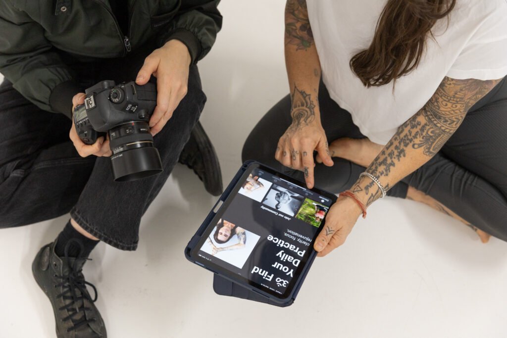 Woman holding a camera while another reviews content on a tablet.