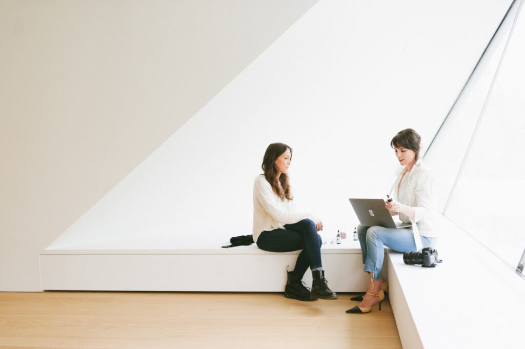 Two women discussing work together with a laptop and camera nearby.