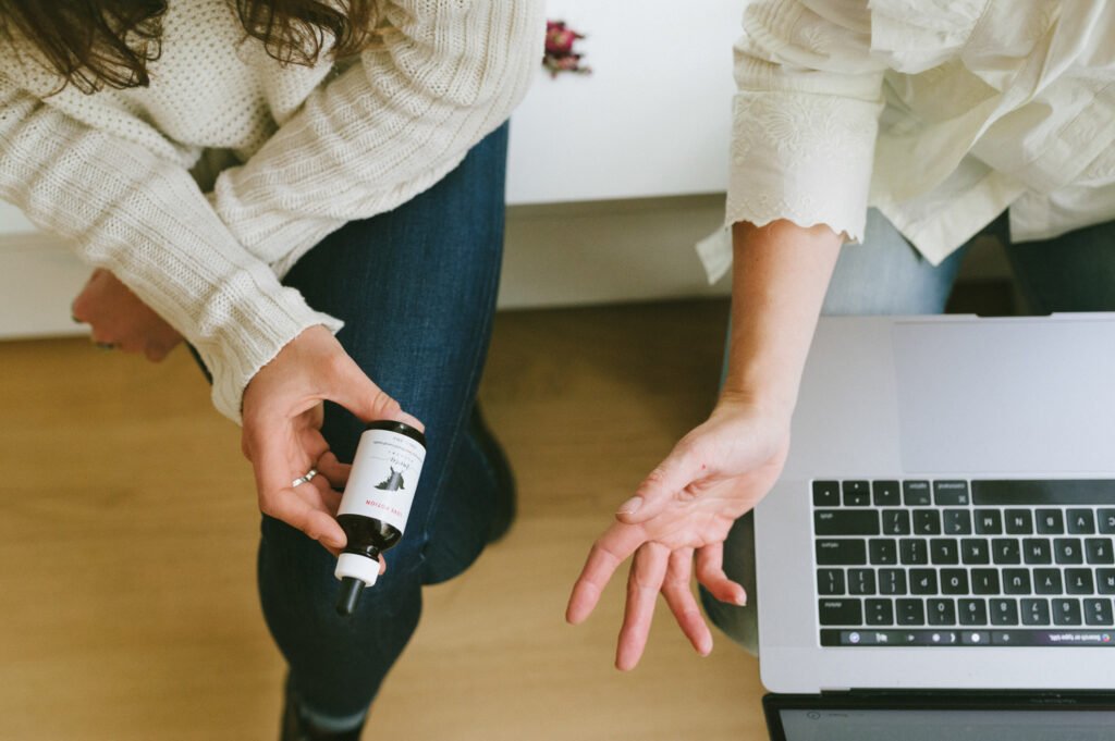 Person holding a small bottle beside a laptop on the floor.