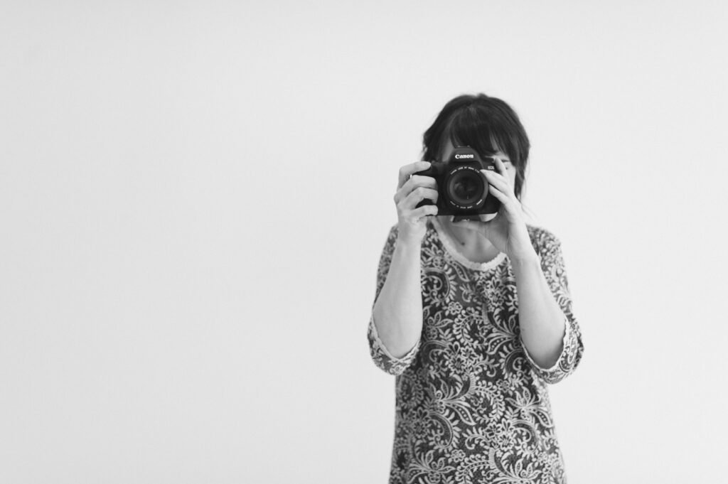 Woman photographing with a Canon camera against a plain white background.