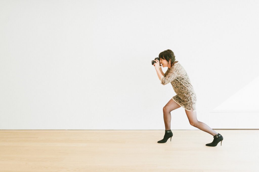 Woman photographing while walking across a bright studio floor.
