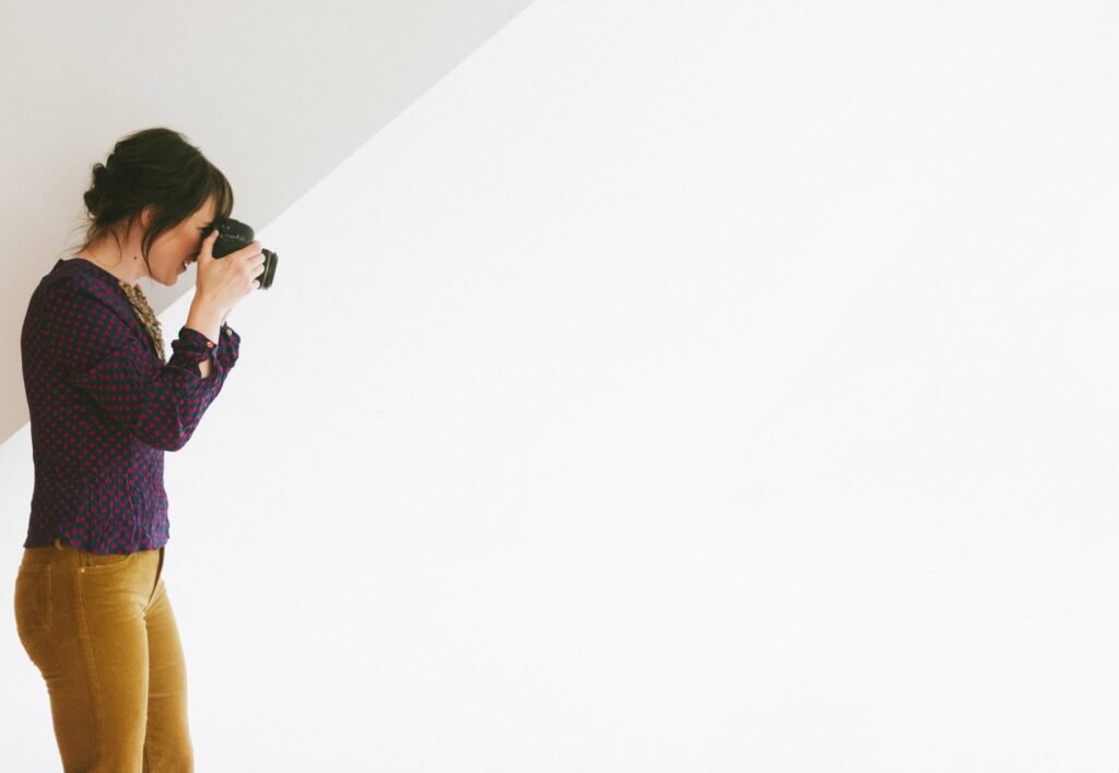 Woman photographing against a bright white wall in a studio